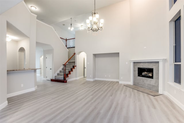 unfurnished living room with a fireplace, light hardwood / wood-style flooring, a high ceiling, and a chandelier