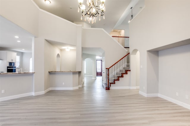 unfurnished living room with a towering ceiling, light hardwood / wood-style flooring, and a chandelier