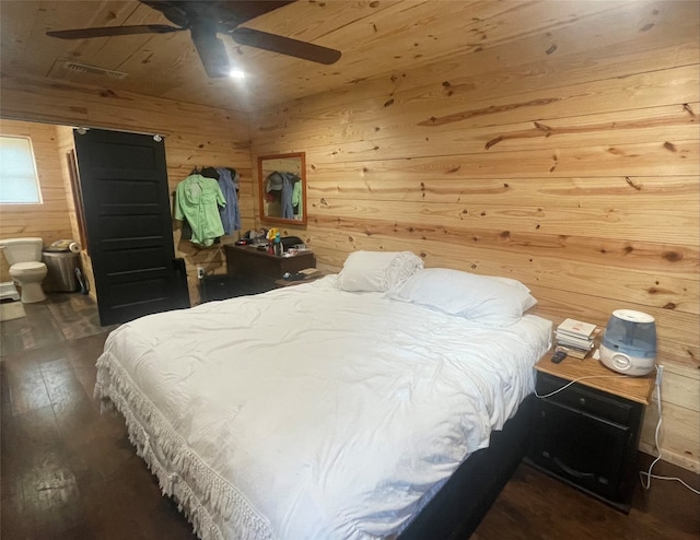 bedroom with dark hardwood / wood-style flooring, connected bathroom, ceiling fan, and wood walls