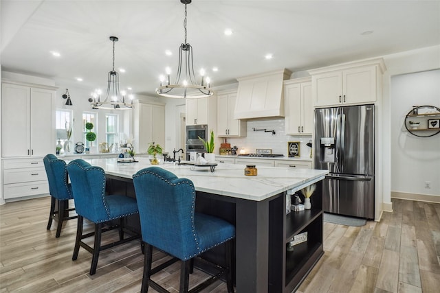 kitchen with light stone counters, stainless steel appliances, premium range hood, a spacious island, and white cabinets