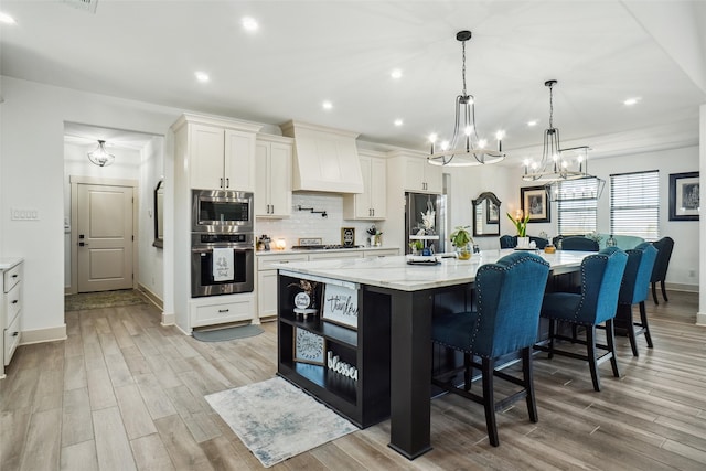 kitchen featuring hanging light fixtures, premium range hood, a spacious island, white cabinets, and appliances with stainless steel finishes