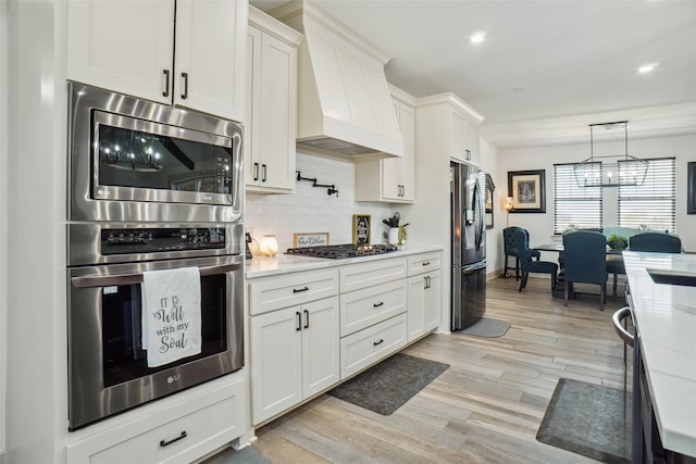 kitchen with premium range hood, light stone countertops, appliances with stainless steel finishes, light hardwood / wood-style floors, and white cabinetry