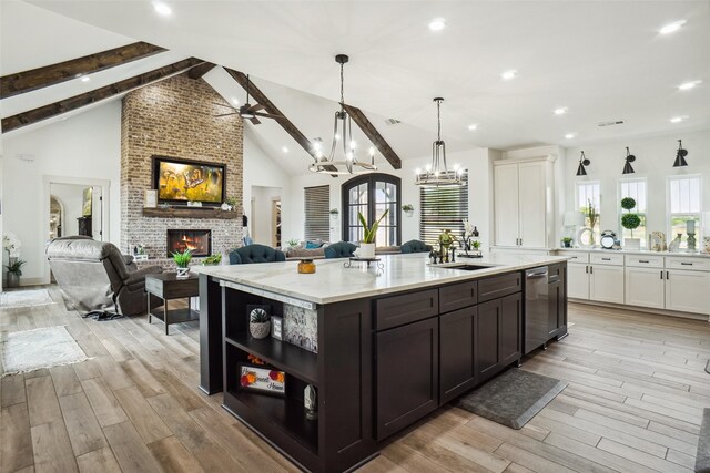 kitchen with a kitchen island with sink, hanging light fixtures, a fireplace, beam ceiling, and light stone counters