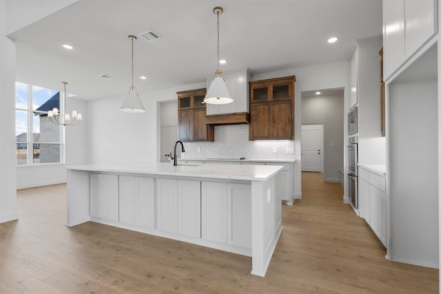 kitchen featuring decorative backsplash, a center island with sink, stainless steel microwave, light wood-type flooring, and pendant lighting