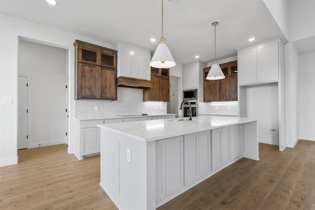 kitchen with appliances with stainless steel finishes, light hardwood / wood-style floors, decorative backsplash, white cabinetry, and a center island with sink