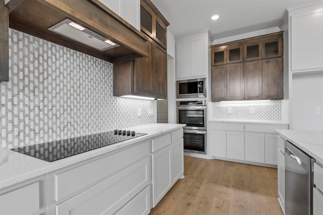 kitchen with decorative backsplash, light stone countertops, light hardwood / wood-style floors, white cabinetry, and stainless steel appliances