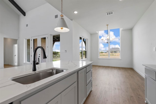 kitchen featuring sink, an inviting chandelier, light wood-type flooring, light stone counters, and hanging light fixtures