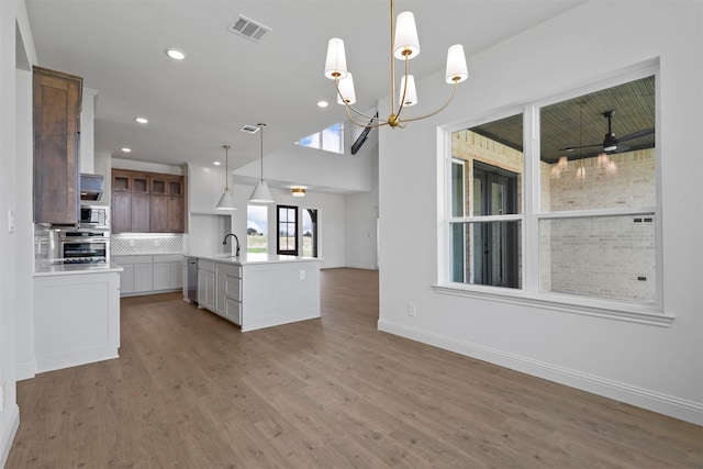 kitchen featuring pendant lighting, hardwood / wood-style floors, white cabinets, a center island with sink, and stainless steel appliances