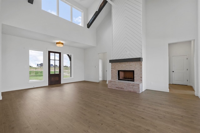 unfurnished living room with a fireplace, high vaulted ceiling, beamed ceiling, and wood-type flooring