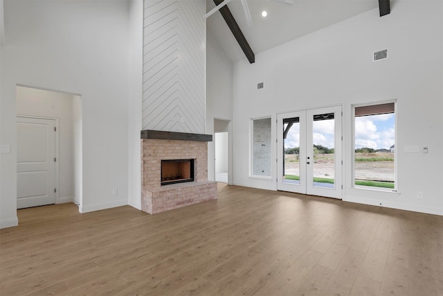 unfurnished living room with high vaulted ceiling, beamed ceiling, and light hardwood / wood-style floors