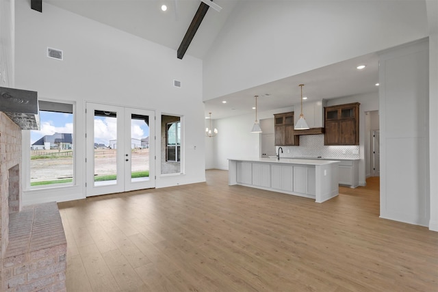 kitchen with decorative light fixtures, beamed ceiling, decorative backsplash, an island with sink, and light hardwood / wood-style floors