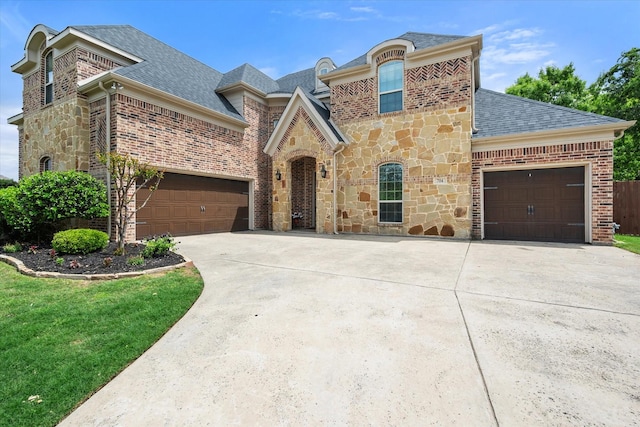 french country style house featuring stone siding, brick siding, driveway, and roof with shingles