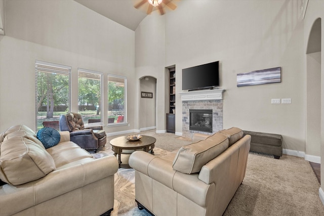 carpeted living area featuring arched walkways, built in features, baseboards, high vaulted ceiling, and a ceiling fan