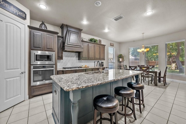 kitchen featuring stainless steel appliances, custom range hood, a sink, visible vents, and a notable chandelier