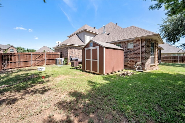 back of house featuring a fenced backyard, an outdoor structure, a storage shed, a lawn, and brick siding