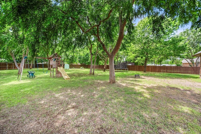 view of yard featuring a trampoline, a fenced backyard, and a playground