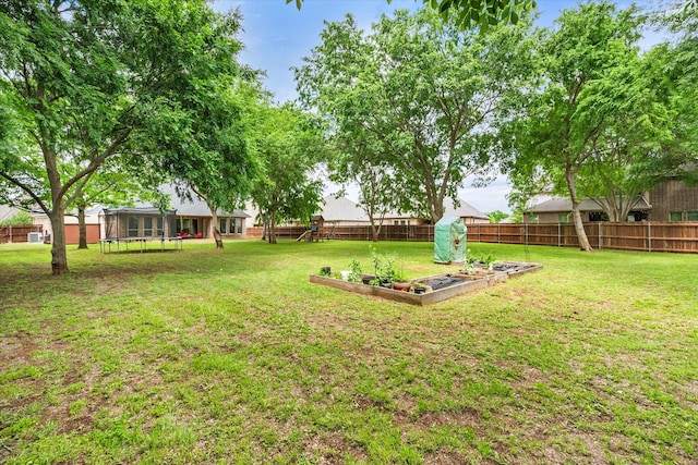 view of yard featuring a trampoline, a vegetable garden, and a fenced backyard