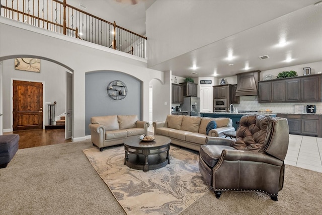 carpeted living room featuring visible vents, a sink, stairway, arched walkways, and a towering ceiling