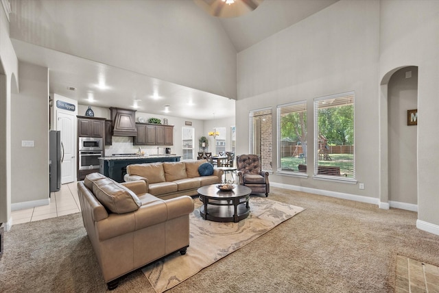 living room with light colored carpet, ceiling fan, arched walkways, baseboards, and high vaulted ceiling