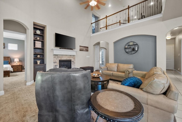 carpeted living room with ceiling fan, baseboards, arched walkways, a brick fireplace, and a towering ceiling