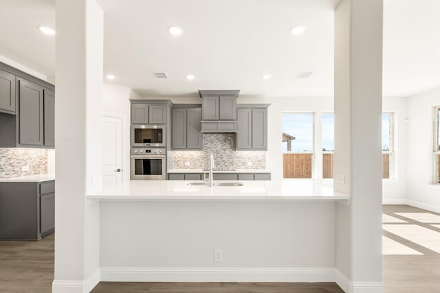 kitchen featuring gray cabinets, kitchen peninsula, sink, and light wood-type flooring