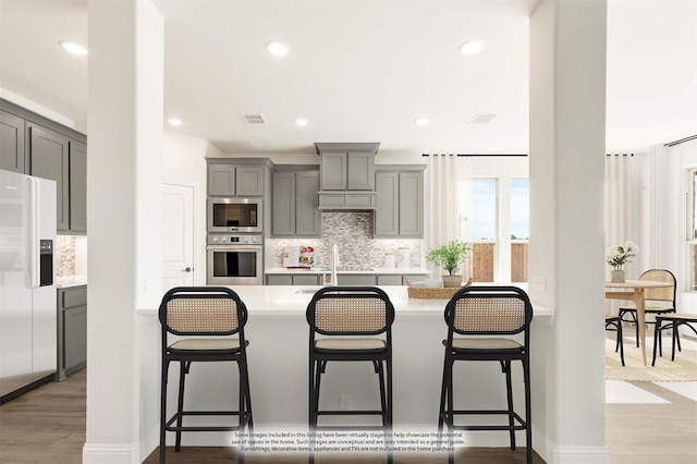 kitchen featuring visible vents, wood finished floors, stainless steel appliances, gray cabinetry, and a kitchen bar