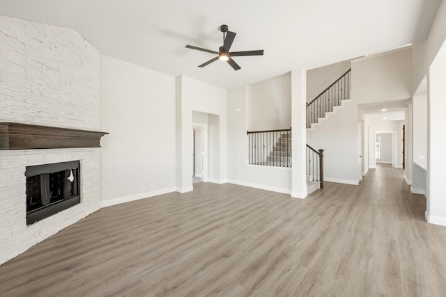 unfurnished living room featuring lofted ceiling, a stone fireplace, light hardwood / wood-style flooring, and ceiling fan