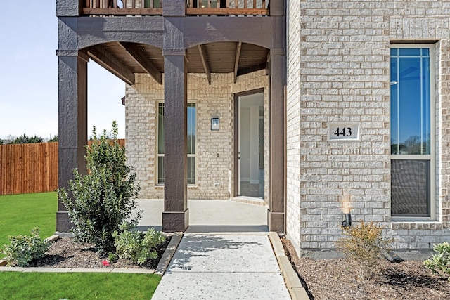 property entrance with a balcony, fence, and brick siding