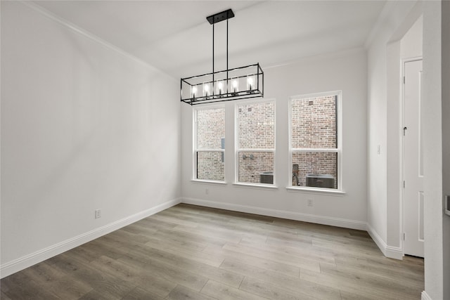 unfurnished dining area featuring ornamental molding, light wood-type flooring, and a notable chandelier