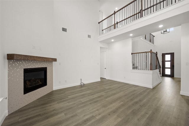 unfurnished living room featuring a tile fireplace, a towering ceiling, and dark hardwood / wood-style floors