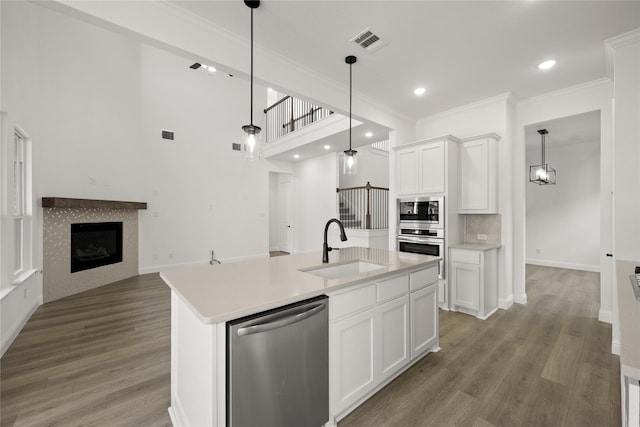 kitchen with stainless steel appliances, a kitchen island with sink, sink, a fireplace, and white cabinetry