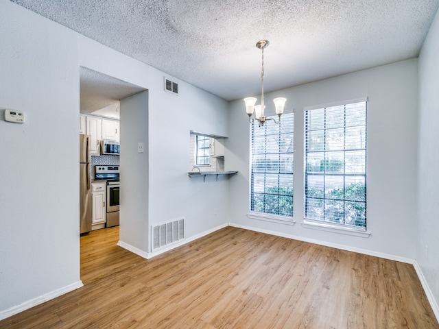 unfurnished dining area featuring light wood-type flooring, an inviting chandelier, and a textured ceiling