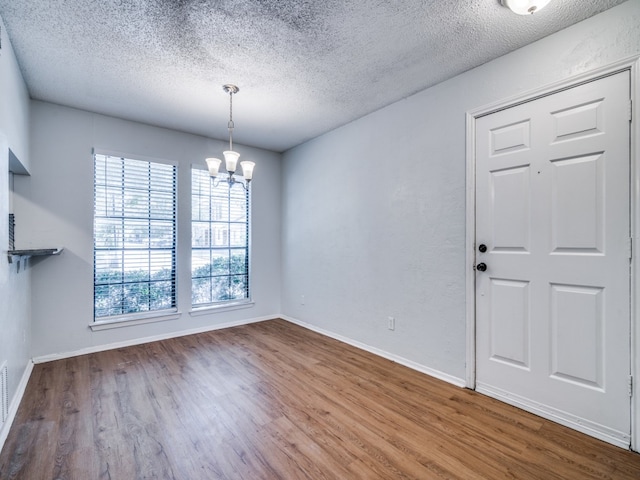 unfurnished dining area featuring a textured ceiling, a notable chandelier, and wood-type flooring