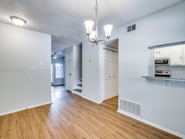 unfurnished dining area featuring light wood-type flooring, a textured ceiling, and ceiling fan with notable chandelier