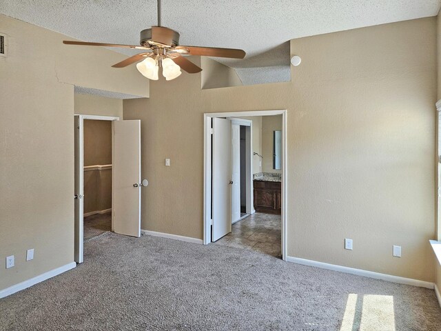 unfurnished bedroom with a textured ceiling, a walk in closet, light carpet, lofted ceiling, and ceiling fan