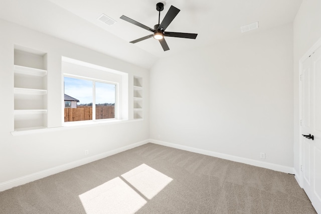 carpeted spare room with ceiling fan, visible vents, baseboards, vaulted ceiling, and built in features