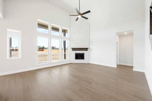 unfurnished living room with ceiling fan, high vaulted ceiling, a fireplace, wood finished floors, and baseboards