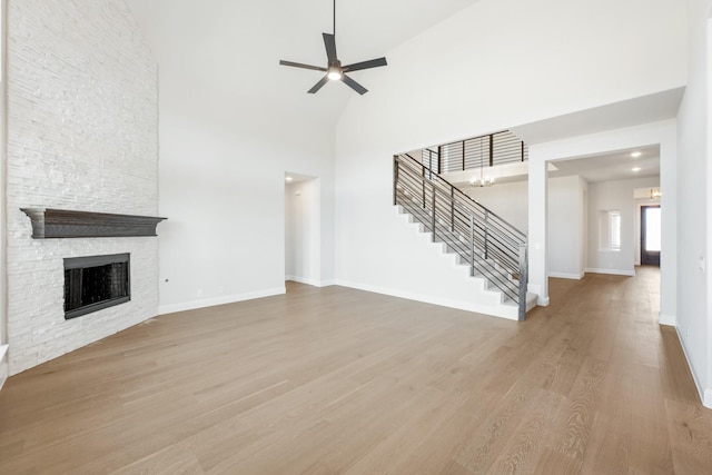 unfurnished living room with a fireplace, a towering ceiling, wood finished floors, baseboards, and stairs