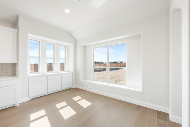 interior space with light wood-type flooring, a wealth of natural light, lofted ceiling, and baseboards