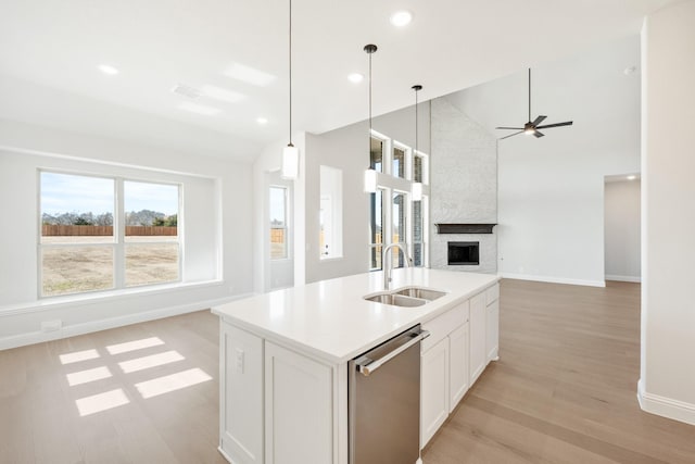 kitchen with dishwasher, an island with sink, open floor plan, a fireplace, and a sink