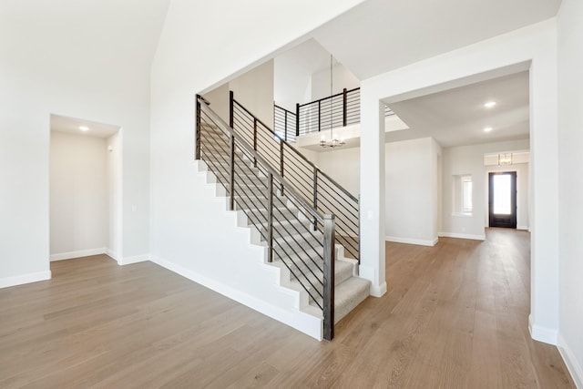 stairs featuring a notable chandelier, recessed lighting, a high ceiling, wood finished floors, and baseboards