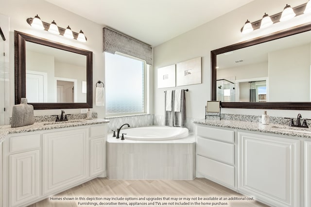 bathroom with a wealth of natural light, tiled bath, and vanity