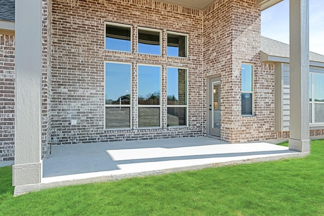 entrance to property featuring brick siding, a lawn, and a shingled roof