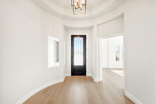 foyer with light wood-type flooring, a notable chandelier, and baseboards