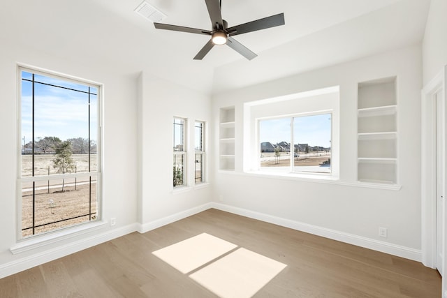 spare room featuring built in shelves, wood finished floors, visible vents, and baseboards