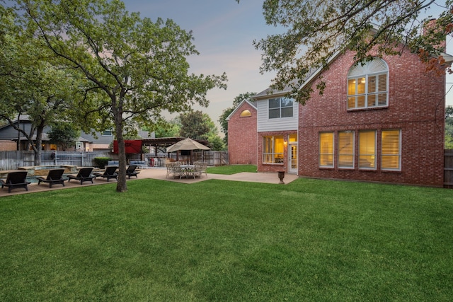 back house at dusk with a patio and a lawn