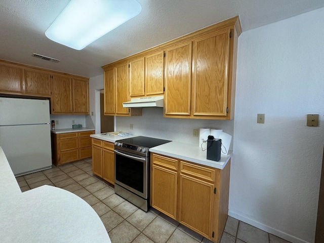 kitchen with under cabinet range hood, stainless steel range with electric cooktop, light countertops, freestanding refrigerator, and brown cabinets