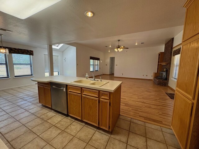 kitchen featuring light countertops, open floor plan, a kitchen island with sink, a sink, and dishwasher