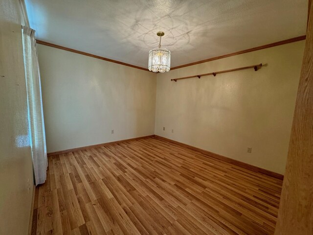 empty room with crown molding, a notable chandelier, baseboards, and wood finished floors