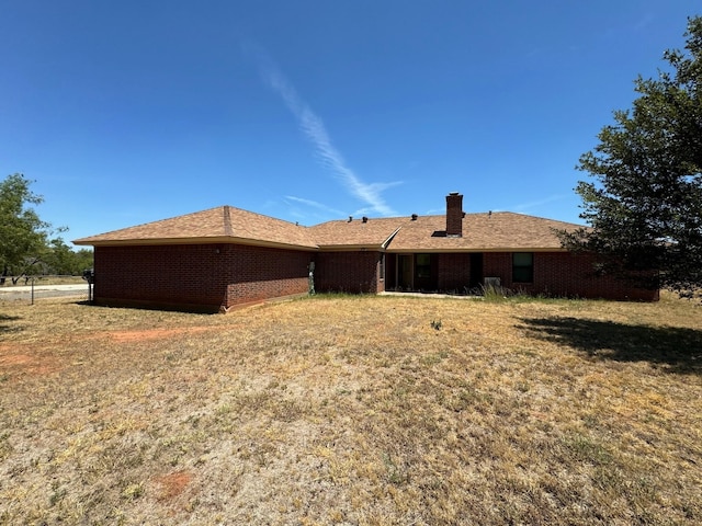 rear view of house with a yard, a chimney, and brick siding